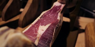 Jamon塞拉诺。传统西班牙火腿在市场上收市。桌上的猪腿火腿。餐厅内部的美食肉。整个火腿放在架子上。摄像机从右向左移动