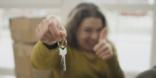 快乐的女人翘起大拇指，展示新的房子钥匙
