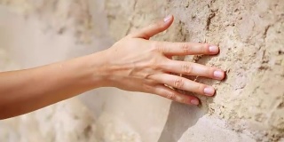 女人的手在古老的石墙上移动。滑动。性感动人。坚硬的石头表面