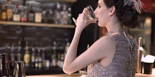 一个20世纪20年代风格的年轻迷人的女人在酒吧喝葡萄酒或香槟的特写。画着漂亮妆容的模特