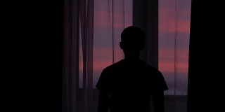 夕阳西下，一个年轻人拉开窗帘的剪影