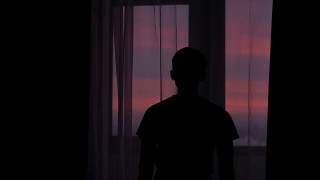 夕阳西下，一个年轻人拉开窗帘的剪影视频素材模板下载