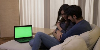 一对夫妇在客厅看惊悚电影，房间里的笔记本电脑上有绿色的屏幕，他们拥抱着大笑