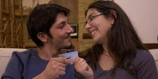 年轻多情的夫妻坐在家里的沙发上向妻子索要信用卡