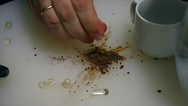这名男子断开了凝胶状的药片，将其中的药片洒在了桌子上。一种干燥的褐色物质从其中沉淀出来。然后，他把药溶解在一杯水里。