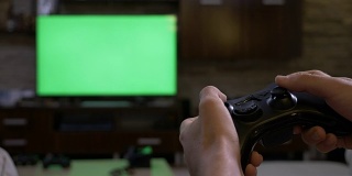 男子手握游戏手柄在色度键前绿色屏幕等离子显示屏上玩游戏机上的视频游戏