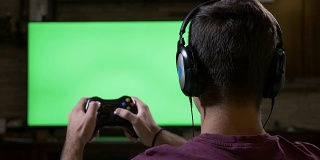 青少年用耳机使用游戏控制器在绿色屏幕电视机前玩单人动作游戏