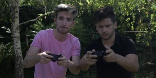 慢镜头，两个年轻的朋友在外面的公园里用控制器玩电子游戏上瘾了