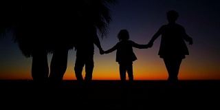 妈妈，爸爸和两个孩子在海滩上散步。夕阳下一家人的剪影。浪漫的周末