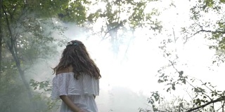 神秘的天使女孩穿着白色的裙子在森林的树木中旋转