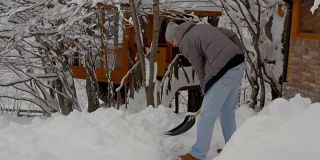 在一个大雪纷飞的寒冷早晨，一名男子拿着铲子正在清除院子里的积雪，