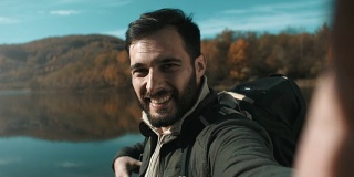 男人拿着相机，拍摄并指着湖面