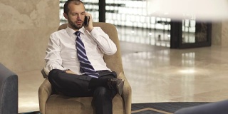 一位时尚的商人坐在酒店大堂或办公室里使用手机。