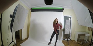 一个年轻的摄影师在一个白色背景的工作室里用数码相机为女性时尚编辑拍摄专业照片的观点