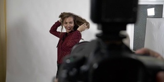 慢动作摄影师的观点POV性感的年轻女孩通过她的长金色卷曲的头发在摄影会议期间在一个专业的工作室