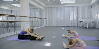 首席芭蕾舞演员教两个孩子如何在宽敞明亮的体育馆里伸展腿