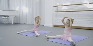 在舞蹈教室里，两个女孩坐在垫子上学习做动作