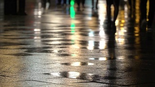 在潮湿的人行道上，街灯映出了辨认不出的人的剪影。长长的影子。雨夜的城市街道上有路灯，沥青路从雨中闪闪发光。不认识的行人，年轻人。夜晚的城市下雨。购物的概念视频素材模板下载
