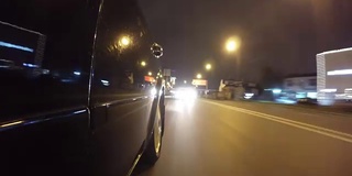 快速城市驾驶夜间道路POV通过城市在夜间时间推移左侧的汽车。低角度的观点。相机拍摄回来