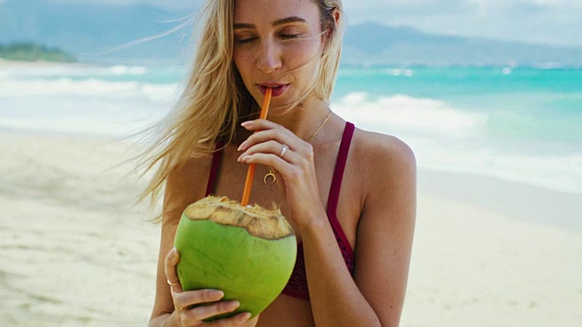 美丽的女孩在海滩上喝椰子