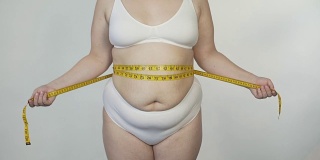 肥胖妇女测量她的腰围在白色内衣，动机和节食