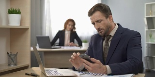 西装男检查手机，在笔记本电脑上输入数据，办公室工作，分心
