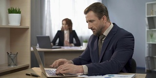 一名男子在笔记本电脑上完成打字，坐在办公桌前，表现超出预期