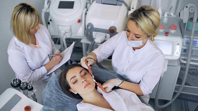 美容师使程序微电流疗法的面部皮肤的一个美丽，年轻的女人在美容院