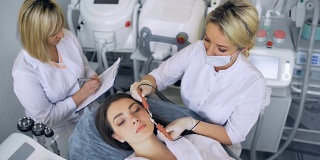 美容师使程序微电流疗法的面部皮肤的一个美丽，年轻的女人在美容院