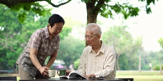 亚洲退休老年夫妇在公园喝咖啡和看书