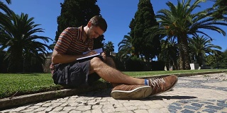 年轻人坐在草坪上，在笔记本上写字，学生做笔记，教育
