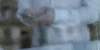抑郁的离婚男人用智能手机发短信，雨水落在窗户玻璃上