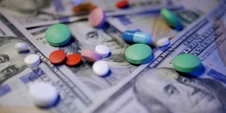 药丸落在钞票上，昂贵的药品，制药生意。药店的主题。多色药片和胶囊的钞票。慢动作