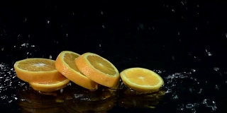 橙子掉进水里就会分解成几片。黑色背景。慢动作