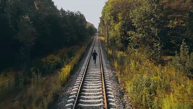 在秋天森林铁路上奔跑的人。无人机的后视图。运动员在道路上清晰的视野地平线。电影的拍摄