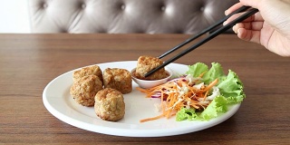 在餐馆的木桌上，女人用筷子夹着一盘“Hoi Jor”，蘸上特制的酱汁。由蟹肉制成的泰中名菜。