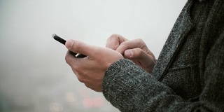 男性手握触屏手机的特写视图。一名年轻人在雾中使用智能手机