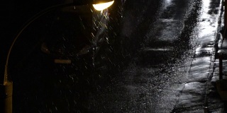 夜间有暴风雪。鸟瞰图。雪在灯下飘落。过往汽车的前灯反射在潮湿的柏油路面上。积雪覆盖在车顶上