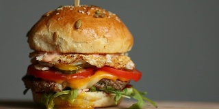大汉堡配牛肉片，番茄，蘑菇，黄瓜和融化的奶酪在木板上旋转，背景光线