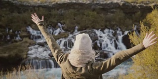 年轻的旅行妇女举起双手，欣赏冰岛瀑布的美丽景色