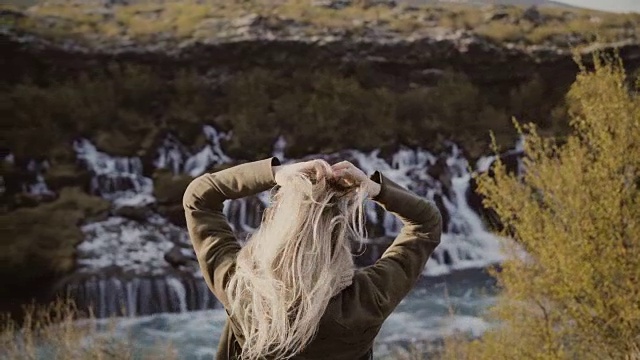 年轻的旅行女人的背影站在山谷和看瀑布在冰岛独自