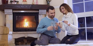 女孩向坐在壁炉旁地板上的丈夫展示怀孕测试