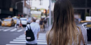 年轻美丽的女人在纽约过马路的背影，美国。女性看乘坐的汽车和出租车