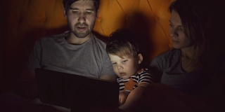 快乐的家庭，小儿子晚上躺在家里的床上学习玩平板电脑