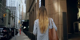 年轻的女商人走过纽约金融区，美国办公室的背影。慢动作