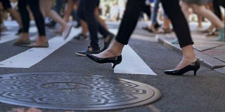 近景时尚女性的脚。女商人正在拥挤的市中心过马路。慢动作