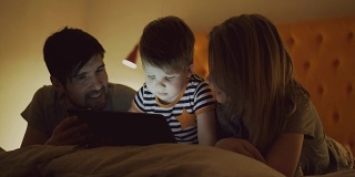 快乐的家庭，小儿子晚上躺在家里的床上学习玩平板电脑