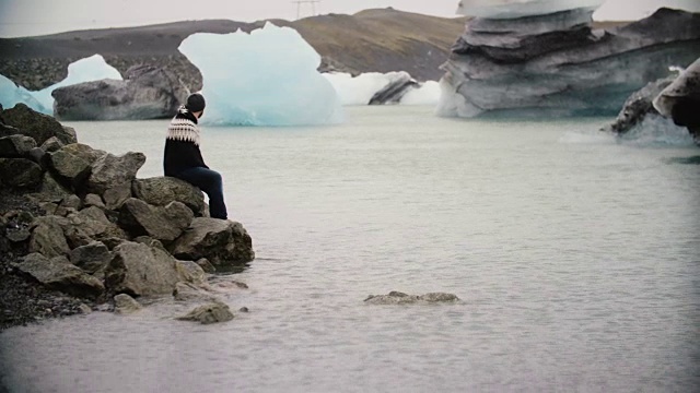 年轻英俊的男子坐在冰礁湖的岩石上欣赏风景。独自探索冰岛的男性