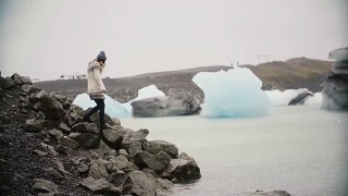 lopapeysa的年轻美女站在冰泻湖上。游客独自探索冰岛的著名景点视频素材模板下载