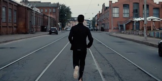 一个运动员在马路中间跑步。背景拍摄。缓慢的运动。回望电车轨道之间的远处景色